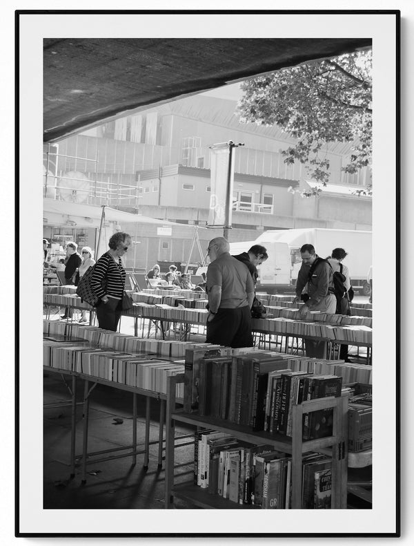 Black and white photograph of the South Bank book market under Waterloo Bridge, London, browsers browsing second-hand books