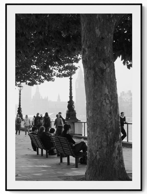 Black and white street photograph of London South Bank, figures walking with the Thames and Parliament behind them